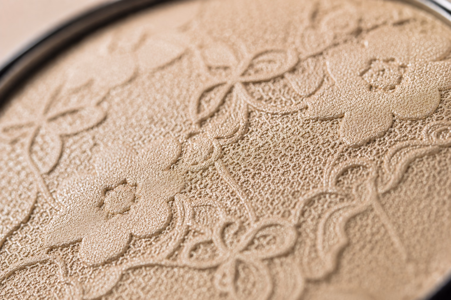 Close-up of champagne-toned cosmetic powder with an embossed floral motif.
